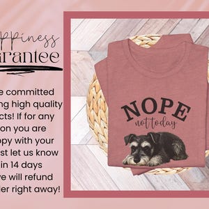 May include: A dusty rose t-shirt with the words "NOPE not today" above a Schnauzer dog illustration. The shirt is folded on a woven basket, set against a light wood-grain background. The image is framed with a dark pink border.