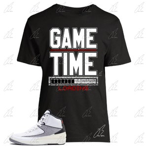 May include: Black t-shirt with white text that reads "GAME TIME" and a loading bar graphic. A pair of white and grey sneakers with black accents.