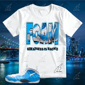 May include: White t-shirt with a blue and white graphic of a sneaker and the word "FOAM". Below the graphic, the text reads "GREATNESS IS BACK!!". A matching blue and white sneaker is in the foreground.