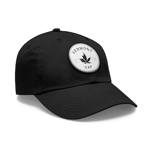 May include: Black baseball cap with a curved brim. A circular patch on the front displays the text "VERMONT SAP" around a maple leaf design. The patch is white with black text and a black leaf.