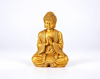 Peut inclure: Une statue de Bouddha dorée en position assise en lotus, les mains jointes en signe de prière. La figurine présente une coiffure texturée, des robes drapées avec des bordures à motifs complexes et une expression faciale sereine.
