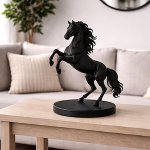 May include: A black horse sculpture rearing up on a round black base. The statue is on a light wood table. The background includes a sofa and a green plant.