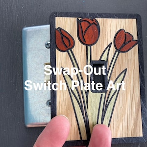 Puede incluir: Placa de interruptor de madera con un diseño floral con tres tulipanes rojos con hojas verdes. La placa tiene un borde negro y el texto "Swap-Out Switch Plate Art".