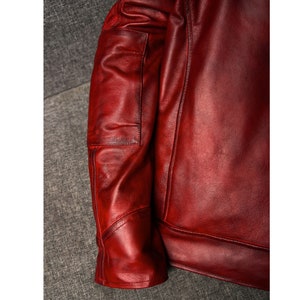 May include: A close-up of a red leather jacket with a zippered pocket on the left sleeve.
