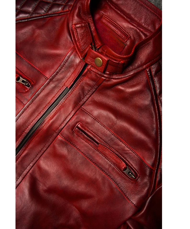 May include: A close-up of a red leather jacket with a zipper closure and multiple pockets. The jacket has a quilted design on the shoulders and a stand-up collar.