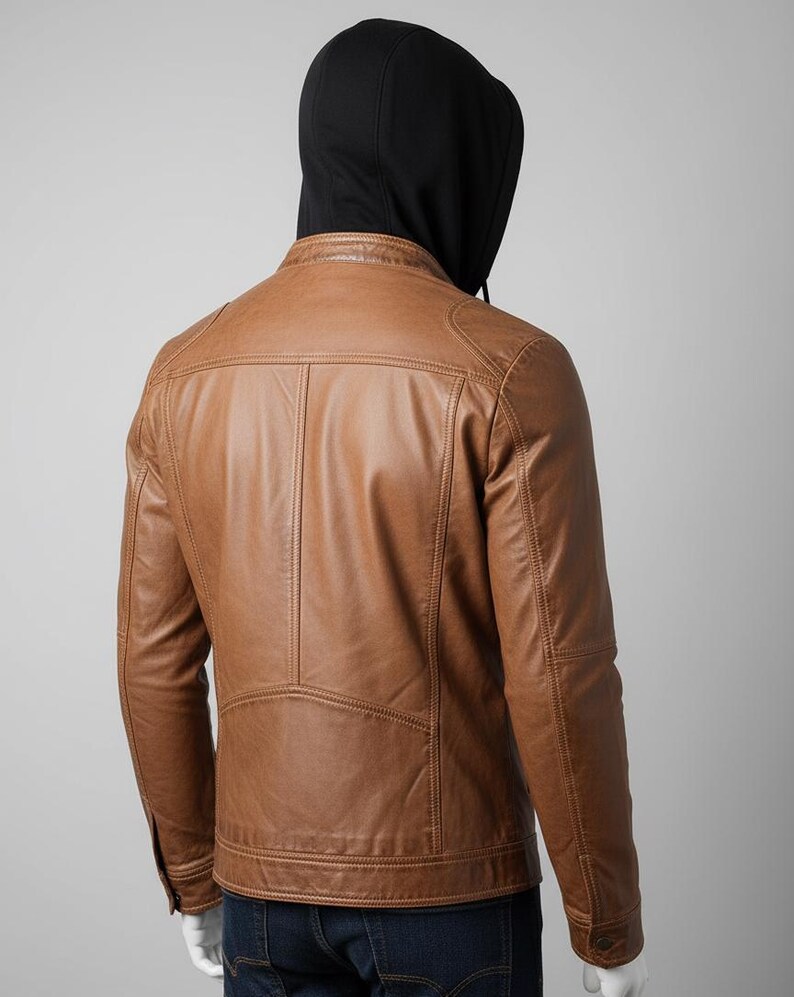 May include: A brown leather jacket with a black hooded sweatshirt underneath. The jacket has a classic design with a stand-up collar, shoulder panels, and vertical stitching details. The jacket is a medium brown color.