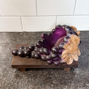 Peut inclure: Sculpture décorative en forme de grappe de raisin, avec des raisins violets foncés et une feuille sculptée. Les raisins sont disposés sur une petite base rectangulaire en bois, créant une pièce de décoration unique.