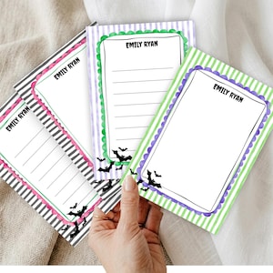 May include: Three rectangular notepad sheets featuring the name EMILY RYAN at the top. Each sheet has a distinct striped background in black, purple, or green, a scalloped border, and black bat illustrations at the bottom corners of the writing area.
