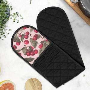 Puede incluir: Manopla de horno acolchada negra con estampado de cerezas. La manopla tiene un exterior negro acolchado y un interior rosa con un diseño de cerezas y hojas. Diseñada para proteger las manos del calor al manipular utensilios de cocina calientes.