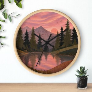 May include: A round wall clock with a light wood frame featuring a printed landscape scene of a lake, pine trees, and mountains under a pink sunset sky. The clock face has black hour, minute, and second hands centered over the illustration.