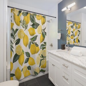 May include: A white shower curtain with a lemon print. The lemons are yellow and the leaves are green. The shower curtain is hanging in a bathroom with a white vanity and a mirror.