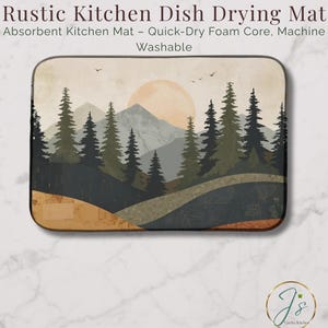May include: Rectangular kitchen dish drying mat with a scenic landscape design. The mat features a mountain range, trees, and a setting sun in shades of beige, green, and blue. Text on the mat reads "Rustic Kitchen Dish Drying Mat" and "Absorbent Kitchen Mat - Quick-Dry Foam Core, Machine Washable."