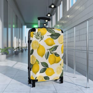 May include: A rolling suitcase with a vibrant lemon pattern. The design features whole and sliced yellow lemons with green leaves on a cream background. The suitcase has a black handle and frame, and is on wheels.