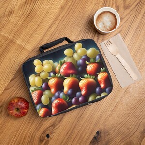 Puede incluir: Una bolsa de almuerzo negra con cierre de cremallera presenta una impresión colorida de fresas, uvas y uvas verdes. La bolsa está hecha de un material duradero y es perfecta para llevar el almuerzo o refrigerios.