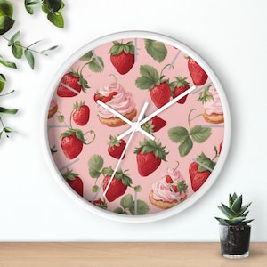 May include: White clock with a pink background and a pattern of strawberries and pink cupcakes. The clock hands are silver.