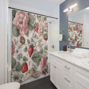 May include: A white shower curtain with a floral pattern featuring pink roses and red strawberries. The shower curtain is hanging in a bathroom with a white vanity and a mirror.