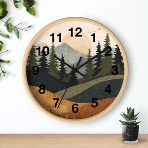 May include: Round wall clock with a light wood frame. The clock face features a landscape design with mountains, trees, and a setting sun. Black numbers mark the hours. The clock hands are black.