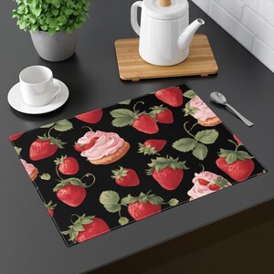 Puede incluir: Salvamanteles negro con un patrón repetido de fresas rojas, hojas verdes y cupcakes rosas y blancos.
