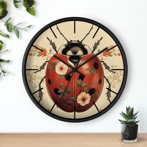 May include: A round wall clock with a black frame. The clock face features a red ladybug design with black spots and floral accents. The background is a cream color with a floral pattern.