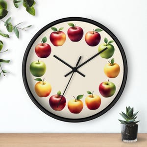 Puede incluir: Un reloj de pared redondo con marco negro y esfera crema. La esfera del reloj presenta un anillo de ilustraciones de manzanas coloridas, cada una con una hoja verde. Las manecillas negras indican la hora.