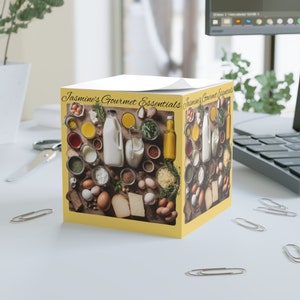 Puede incluir: Una caja amarilla con un collage de artículos gourmet, incluyendo huevos, leche, queso, especias y hierbas. La caja está etiquetada como "Jasmine's Gourmet Essentials".