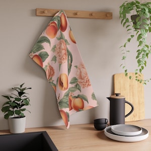 May include: A pink kitchen towel with a peach and floral pattern. The towel is hanging on a wooden rack.