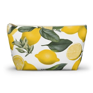 Può includere: Un beauty case bianco con cerniera e motivo a limoni. Il design include limoni interi e a fette, foglie verdi e steli. Il beauty case ha una cerniera dorata e una forma rettangolare. Misura circa 25 cm.