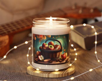 Puede incluir: Un tarro de vidrio para velas con tapa blanca y una ilustración colorida de una cesta de manzanas y palitos de canela. La vela está rodeada de luces blancas.