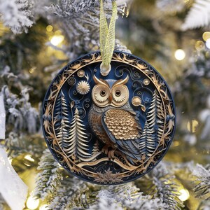 May include: A round Christmas ornament with a detailed owl design. The ornament features a dark blue background with gold and brown accents, including an owl, trees, and decorative elements. It hangs from a gold ribbon.