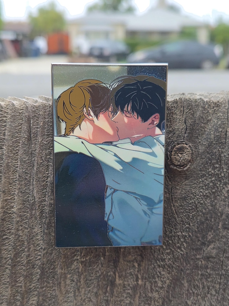 Op de afbeelding: Een rechthoekige pin met een illustratie van twee kussende mensen. E&eacute;n persoon heeft bruin haar, de ander zwart. Het kunstwerk is in mangastijl, met zachte schaduwen en een focus op de gezichten.