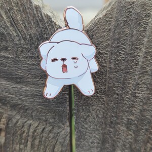 Op de afbeelding: Een lichtblauwe emaille pin in de vorm van een cartoonhond met een verdrietige uitdrukking. De pin heeft een ros&eacute;gouden omtrek en een pin back. De hond huilt en heeft zijn mond open. De pin is bevestigd aan een groene stengel.