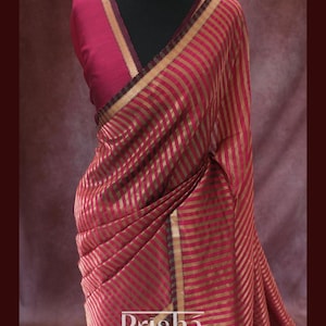 May include: A red and gold striped saree with a matching blouse and a gold necklace. The saree features vertical stripes and is draped on a mannequin. The word "Prisha" is visible on the saree.
