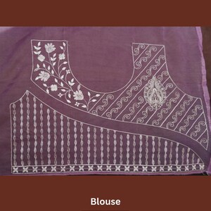 Pu&ograve; includere: Una camicetta lavanda con ricami bianchi intricati. Il design presenta motivi floreali lungo lo scollo e un motivo geometrico dettagliato sul corpetto. La parola "Blouse" e il marchio "Prisha" sono visualizzati in basso.