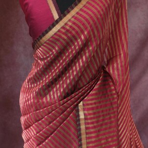 May include: A draped magenta saree with gold stripes and trim, displayed on a mannequin. The saree features the brand name "Prisha" at the bottom. A matching magenta blouse and ornate gold necklace complete the ensemble.