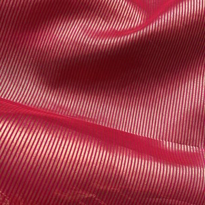 May include: Close-up of a vibrant pink fabric with a subtle sheen. The material features a pattern of thin, vertical, metallic gold stripes, creating a textured and luxurious appearance. The fabric is likely used for apparel or home decor.