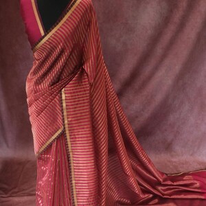 May include: A red and gold striped saree draped on a mannequin. The saree has gold trim and a matching blouse. A gold necklace adorns the mannequin's neck. The word "Prisha" is visible at the bottom of the image.