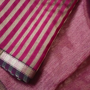 May include: Close-up of a textile with a striped pattern in shades of pink and silver. The fabric has a textured appearance and a decorative border. The word "Prisha" is visible in the bottom right corner.