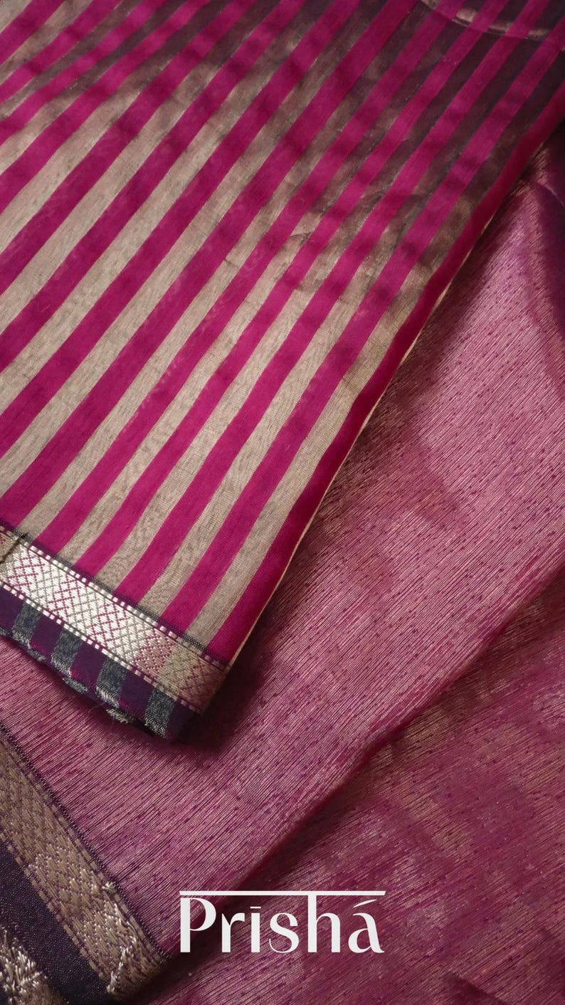 May include: Close-up of a textile with a striped pattern in shades of pink and silver. The fabric has a textured appearance and a decorative border. The word "Prisha" is visible in the bottom right corner.