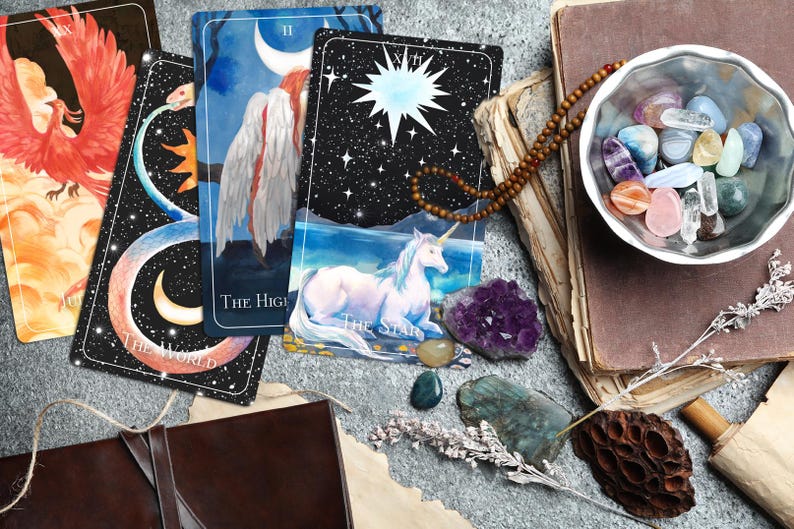 Op de afbeelding: Vier tarotkaarten, De Wereld, De Hogepriesteres, De Ster en XVII De Ster, liggen uitgespreid op een tafel met een kom met kleurrijke kristallen, een boek en een kralenketting.