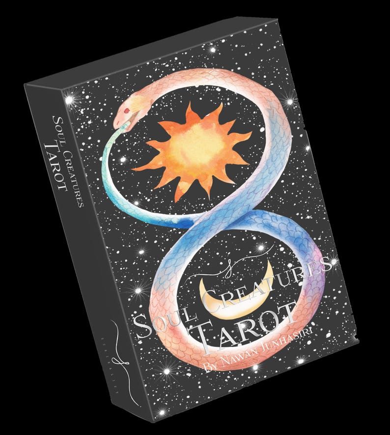 Op de afbeelding: Een zwarte doos met een zilveren ontwerp met een slang die om een zon en maan is gewikkeld. De tekst op de doos luidt "Soul Creatures Tarot by Nawan Junhasiri".