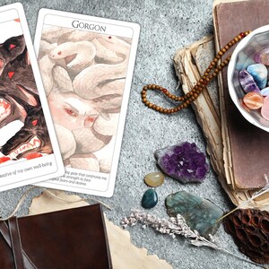 May include: Two tarot cards, one with a three-headed dog called Cerberus and the text "I am fiercely protective of my own well-being", and the other with a Gorgon with snakes for hair and the text "The gaze that confronts me merges my strength to face  expected fears and desires".