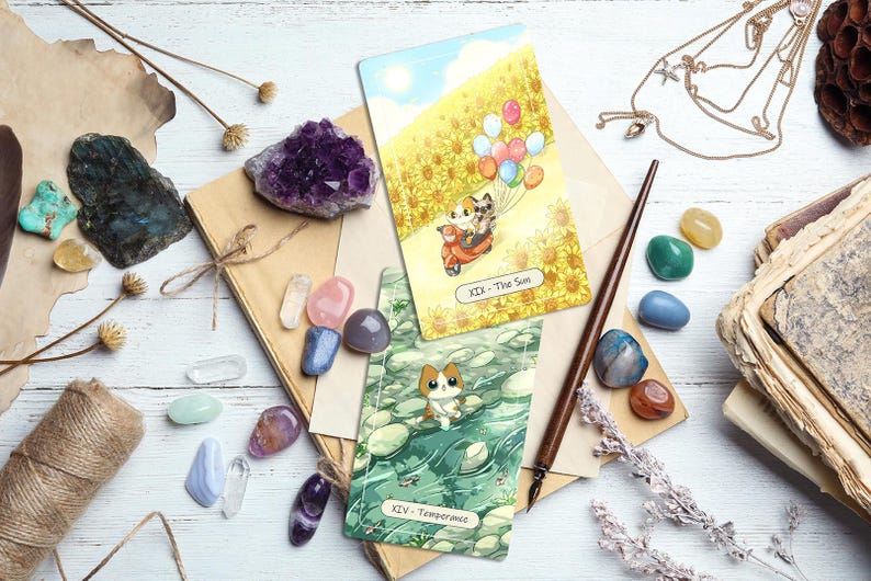 Puede incluir: Vista cenital de una colecci&oacute;n de cartas del tarot, cristales y objetos vintage. Se ven dos cartas del tarot, una que representa un gato en un scooter con globos, la otra un gato en el agua. Varios cristales en tonos morados, rosas, azules y verdes est&aacute;n dispersos.