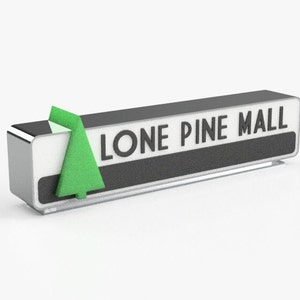 Può includere: Un cartello argentato con un'icona di pino verde e il testo "LONE PINE MALL" in lettere nere.