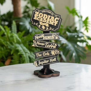 Op de afbeelding: Een zwarte houten wegwijzer met gouden letters met de tekst "Welcome to Zodiac Academy" en "Nolavia". Daaronder staan richtingborden voor "House Ignis", "House Terra", "The Orb" en "Jupiter Hall".