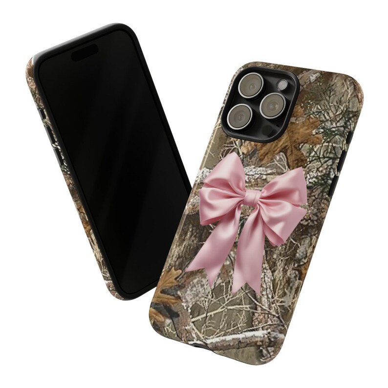 Pode incluir: Uma capa de telefone camuflada com um la&ccedil;o rosa. A capa tem uma borda preta e um recorte para a lente da c&acirc;mera.