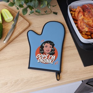 May include: Blue oven mitt with a black border. The mitt features a red circle with a cartoon woman and the text "Oops I'm Drunk!"