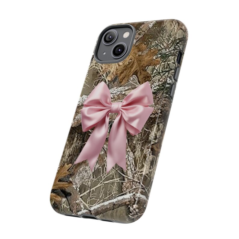 Pode incluir: Uma capa de telefone camuflada com um la&ccedil;o rosa. A capa &eacute; projetada para um iPhone.