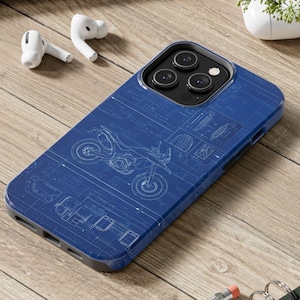 May include: A blue phone case with a motorcycle blueprint design. The case has a dark blue border and a detailed white outline of a motorcycle. The case is on a wooden surface with white earbuds and a small white container in the background.