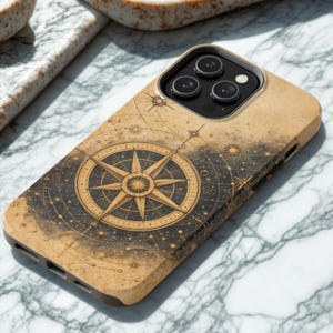 May include: A phone case with a compass rose design. The case has a tan background with a dark compass rose in the center, surrounded by celestial elements. The case is designed to fit a smartphone with three camera lenses.