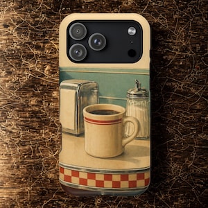 Könnte beinhalten: Handyhülle mit einer Diner-Szene mit einer Kaffeetasse, einem Zuckerspender und einem Serviettenhalter. Die Tasse hat rote Streifen. Die Hülle hat einen cremefarbenen Rand und ein braun-rotes Karomuster.